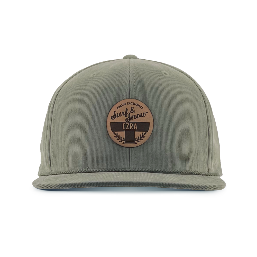 Olive green corduroy cap with a brown leather patch on a white background