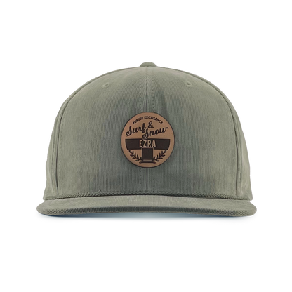 Olive green corduroy cap with a brown leather patch on a white background